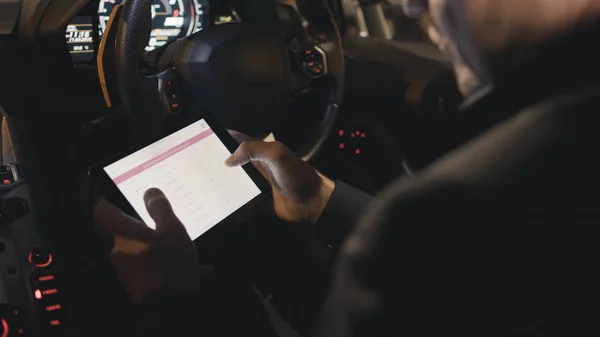 Primer plano de las manos usando tableta digital mientras está sentado en un coche. Acciones. Empresario comprueba las acciones en la tableta en el coche — Foto de Stock