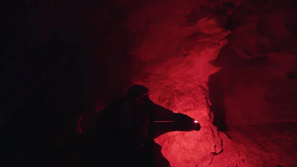 Hombre caminando dentro de la cueva subterránea mística con una llamarada de señal roja ardiente en el fondo de las paredes oscuras. Imágenes de archivo. Senderista explorando camino desconocido . — Foto de Stock