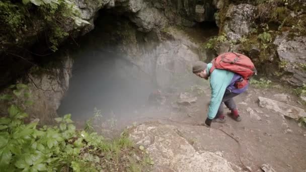 Reiziger daalt af naar de grot. Voorraadbeelden. Explorer met verzekering daalt steile afdaling naar donkere mistige grot in rots. Extreme buitenactiviteiten — Stockvideo