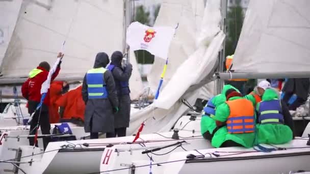 Lidé připravují bílé lodě pro plachtění a soutěže ve větrném počasí, sportovní koncept. Umění. Mnoho lidí v čistých šatech a pláštěnkách stojí v jachtách. — Stock video