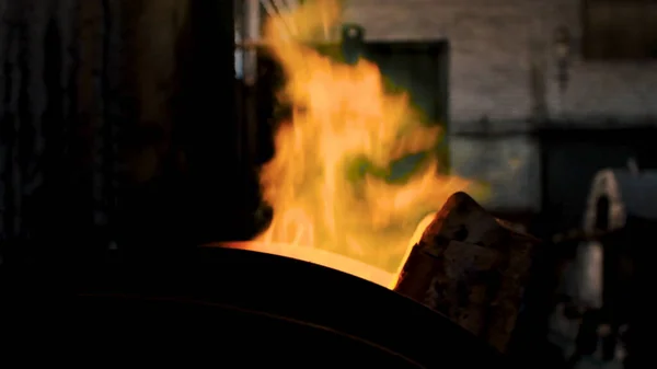 Nahaufnahme eines brennenden Feuers aus dem Ofen in der dunklen Werkstatt der Fabrik. Kunst. leuchtend orangefarbenes und grünes Feuer brennt während des Schmelzprozesses, — Stockfoto