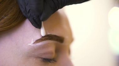 Kadın müşteri kaşının kenarından boyayı ve özel beyaz macunu çıkaran usta bir elin yakın çekimi. - Sanat. Güzellik salonunda estetik ameliyat..