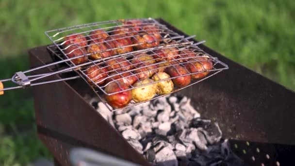 Tæt på rå kartofler på grillen udendørs på grøn medow baggrund, vegetarisk måltid. Kunst. Lækker picnic i en sommersolrig dag . – Stock-video