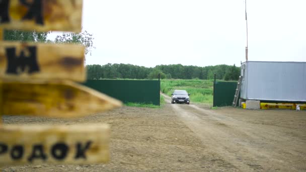 Sommerlandschaft mit einem Dorfplatz und einem Auto, das durch das grüne Tor zum Hof fährt. Kunst, Fahrzeugfahren im Grünen auf Wald- und Wiesenhintergrund. — Stockvideo