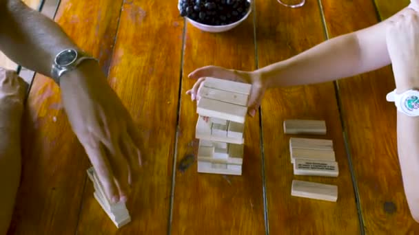 Nahaufnahme eines Ehepaares, das drinnen auf einem Holztisch Jenga spielt. Kunst. Draufsicht der Hände, die Holzklötze halten, Jenga-Spiel . — Stockvideo
