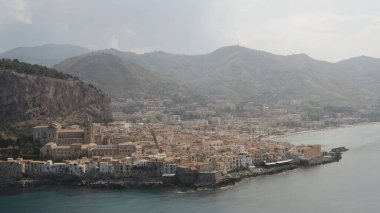 Dağların yakınındaki bulutlu gökyüzü arka planında bir kıyı kasabasının havadan panoramik görüntüsü. Başla. Deniz kıyısının ve küçük kasabanın güzel manzarası.