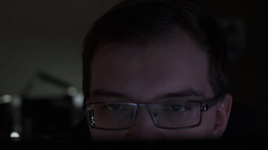 Karanlık odada otururken monitöre bakan genç işadamlarının yakın çekimi. Stok görüntüleri. Gözlüklü bir adam bilgisayar ekranına bakıyor..