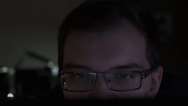 Close-up of young businessman looking at monitor while sitting in the dark room. Stock footage. Man wearing glasses looking at computer screen. — Stock Photo, Image