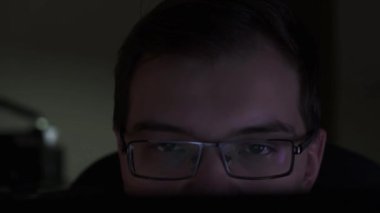 Karanlık odada otururken monitöre bakan genç işadamlarının yakın çekimi. Stok görüntüleri. Gözlüklü bir adam bilgisayar ekranına bakıyor..