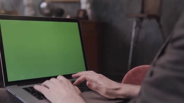 Over de schouder van een man die aan zijn bureau zit en werkt aan een laptop met Green Screen. Beelden van aandelen. Man met behulp van notebook computer met chroma sleutel. — Stockvideo