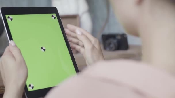 Ahşap masa arkasında yeşil ekranlı tablet tableti tutan bir kadının yan görüntüsü. Stok görüntüleri. Krom anahtarlı Ipad kullanan bir kıza yaklaş. — Stok video