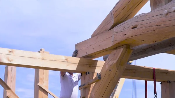 Travailleur sur le chantier pendant le processus de construction d'une maison en bois sur fond bleu ciel nuageux. Clip. Menuisiers hommes au travail avec maison en bois rond . — Photo