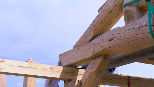 Travailleur sur le chantier pendant le processus de construction d'une maison en bois sur fond bleu ciel nuageux. Clip. Menuisiers hommes au travail avec maison en bois rond . — Photo