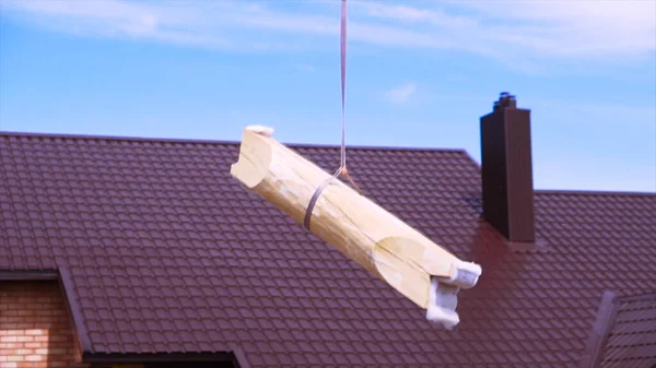 Tronco corto colgado en una cuerda de construcción sobre fondo azul nublado del cielo. Clip. Materiales para el edificio de casa de madera . —  Fotos de Stock