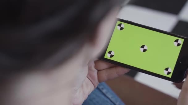 Vrouwelijke tiener meisje met donker haar met behulp van smartphone met groen scherm, binnen zitten. Voorraadbeelden. Vrouw met Iphone met chroma sleutel in horizontale positie. — Stockvideo