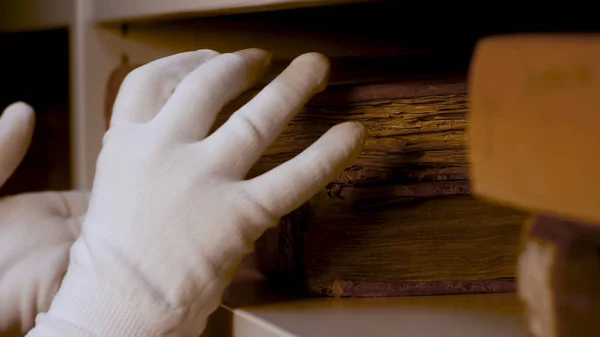 Close up of hands in white gloves putting on a shelve an old antique book very carefully. Stock footage. Ancient book with yellow pages in the storage.