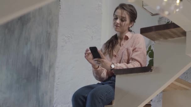 Mujer elegante sentado en las estrellas en su casa de campo mientras lee el mensaje y sonriente, concepto de comunicación en línea. Imágenes de archivo. Mujer bonita con su teléfono celular en casa . — Vídeo de stock