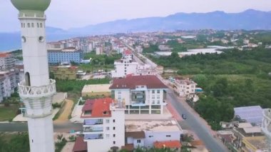 Şehir sokakları, evler, parklar ve yeşil ağaçlarla çevrili bir caminin iki minaresinin havadan görüntüsü. - Sanat. Yaz şehrinin üstündeki minarelerde uçarak.