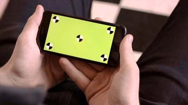 Primer plano del hombre sosteniendo el teléfono con pantalla verde. Imágenes de archivo. El hombre tiene un nuevo teléfono inteligente y mira a la pantalla verde con puntos — Foto de Stock