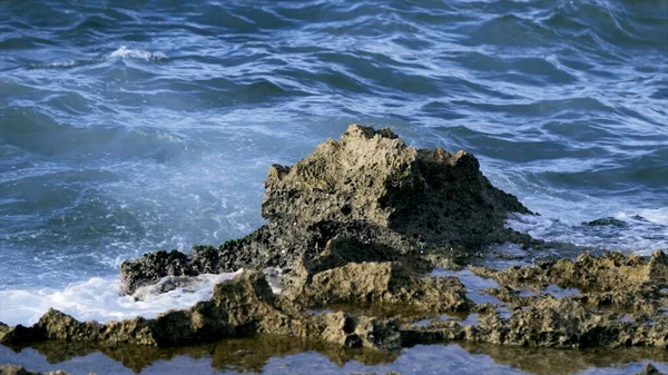 Petites vagues frappant et éclaboussant contre le rivage. L'action. Des vagues frappent le rocher. Des éclaboussures de vagues marines sur de petits rochers — Photo