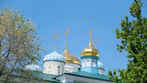 Ortodox kereszt arany kupolák vagy kupolák againts kék tiszta ég. Készletfelvétel. Gyönyörű templom a Mindenszentek tiszteletére, zöld fákkal körülvéve.. — Stock videók