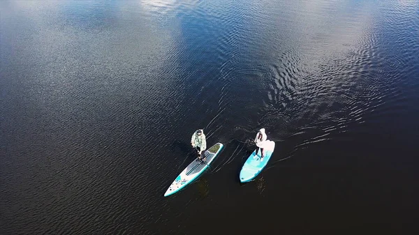 Draufsicht auf ein Paar beim Paddeln auf dem See, Sport- und Lifestylekonzept. Filmmaterial. Antenne eines Mannes und einer Frau, die auf einem Surfbrett stehen und mit einem Paddel rudern. — Stockfoto