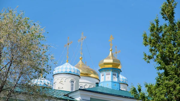 Orthodoxe Kreuze auf goldenen Kuppeln vor blauem Himmel. Archivmaterial. schöne Kirche zu Ehren aller Heiligen umgeben von grünen Bäumen. — Stockfoto