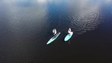 Göl, spor ve yaşam tarzı kavramında kürek çeken bir çiftin en iyi görüntüsü. Görüntü. Sörf tahtasının üzerinde duran ve kürekle kürek çeken bir adam ve kadının havası..