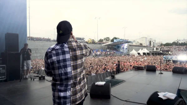 Engeland - Londen, 09.01.2019: achteraanzicht van een zanger die het podium opkomt en zwaait naar zijn fans op rapmuziekfestival. Actie. Jongeman voor het concert buiten. — Stockfoto