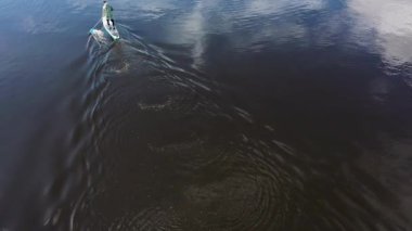 Kürekte kürek çeken bir sporcu, suda açık hava aktiviteleri. Görüntü. Arkasında dalgalar bırakan kürekçi bir adamın havadan görünüşü..