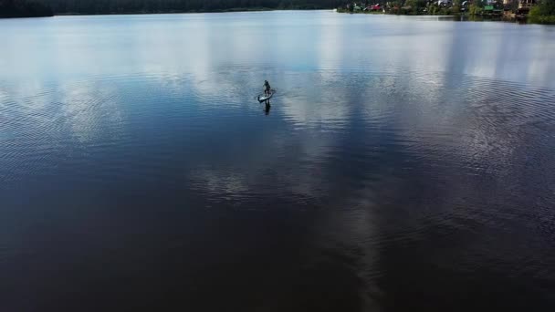 Vue de dessus d'un gars qui fait du paddle board sur le lac, le sport et le style de vie concept. Des images. Aérien d'un homme debout sur une planche de surf et ramant avec une pagaie . — Video