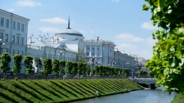 Красивий міський пейзаж з вузьким каналом і двома схилами, вкритими зеленою травою на синьому хмарному фоні неба. Стокові кадри. Літня міська вулиця з білими будинками, і люди ходять по мосту . — стокове відео