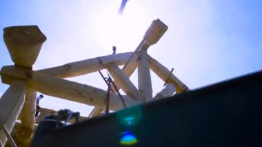 İnşaat alanındaki ahşap kirişin üzerinde oturan bir marangozun alt manzarası, iskelet. Şarjör. Ahşap kütük vinç tarafından taşınıyor..