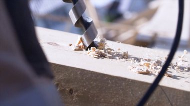 Marangoz matkapla ahşap kirişte delik açar, el işi konsepti, ahşap işçiliği. Şarjör. Çalışan matkabı ahşap talaşıyla kapatın..