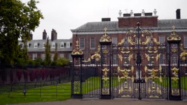 Beautiful gates with gold patterns. Action. Facade of old manor house with green lawn and black graceful gate in cloudy weather. Old estate with beautiful architecture and landscape