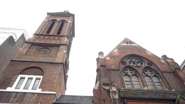 Bottom view of old architectural building of city on background of cloudy sky. Action. Facade of old Gothic Church of dark brick with tower in city — Stock Video