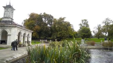 Beautiful green Park with fountains in cloudy weather. Action. Large old Park with pond and fountains on background of walking tourists in cloudy weather