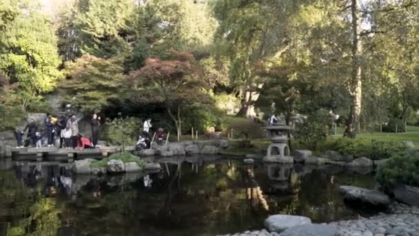 Beau parc national à Londres avec un petit étang et des familles marchant autour sur fond d'arbres verts. L'action. Petit étang entouré de pierres avec le reflet des gens à la surface de l'eau . — Video