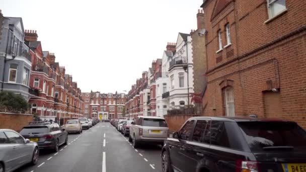London, Britain-September, 2019: Προοπτική του δρόμου με παλιά σπίτια και σταθμευμένα αυτοκίνητα. Πάμε. Όμορφη στενό δρόμο με σταθμευμένα αυτοκίνητα και κόκκινα παλιά σπίτια στο φόντο του συννεφιασμένου ουρανού — Αρχείο Βίντεο