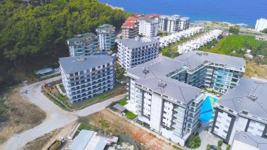 Güzel küçük kasabanın ve sahil beldesinin havadan görünüşü, açık havuzu olan sahil otelleri. Şarjör. Tatil köyü ve inşaat alanının zıt manzarasının üst görüntüsü.