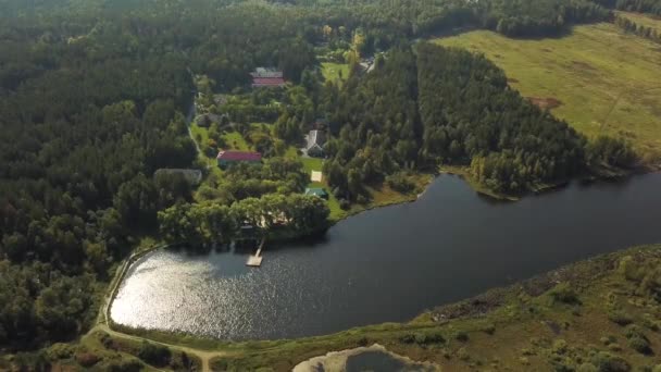 Aerial view of a beautiful small village near the lake and green forest. Stock footage. Top view of modern houses, pine trees, and rippled surface of the lake. — Stockvideo