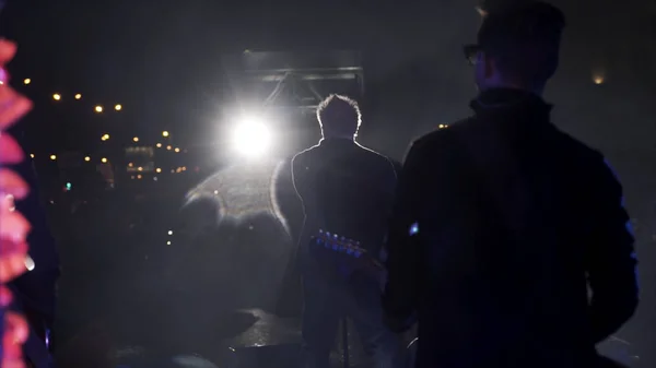 Moscú, Rusia - 11.20.2019: vista trasera del guitarrista y un líder actúan en el escenario del concierto en la sala oscura. Acción. Proyectores de escenario y una banda musical durante el concierto . — Foto de Stock