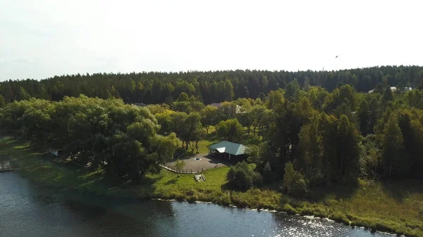 Vidéki folyó egy fa mólóval és egy ház a fák között. Készletfelvétel. A szabadidős bázissal rendelkező ökológiai terület levegője, nyári természet. — Stock Fotó