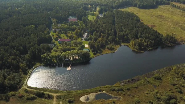 Vista aérea de un pequeño y hermoso pueblo cerca del lago y el bosque verde. Imágenes de archivo. Vista superior de casas modernas, pinos y superficie ondulada del lago . — Foto de Stock