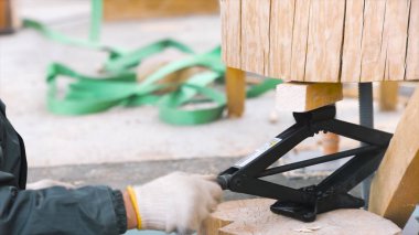 Ahşap ev inşaatı, marangozluk konsepti. Şarjör. Ahşap çerçeve yapısının parçaları arasındaki rombik kaldırma krikosunu gevşeten bir işçiye yaklaş.