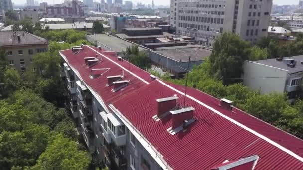 Lucht uitzicht op het felroze dak van meerdere verdiepingen tellend woongebouw onder andere huizen en groene bomen. Voorraadbeelden. Top uitzicht op groene kleine stad in de zomer. — Stockvideo