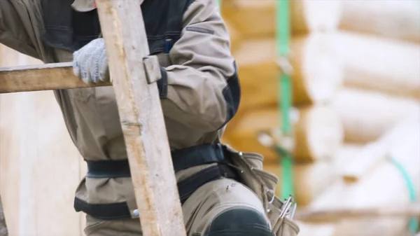 Dekat dari seorang pria mengenakan pakaian memanjat tangga kayu. Jepit. Tukang kayu profesional memanjat tangga di lokasi konstruksi . — Stok Foto