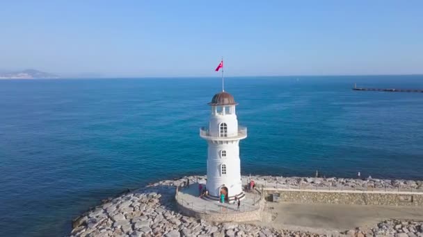 Flyg från fyren nära det blå havet. Konst. Vit vacker fyr med vandrande turister och klar himmel med horisonten på bakgrunden. — Stockvideo