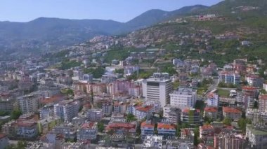 Türkiye 'nin Akdeniz kıyısındaki güneşli Alanya kasabasının üzerinde uçuyor. - Sanat. Dağ yamacının havadan görünüşü evler ve ağaçlarla kaplı..