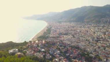 Şehre doğru uçan hava manzarası ve denizin üzerindeki günbatımına karşı bir dağ. - Sanat. Güneş ışığının su yüzeyine yansıdığı inanılmaz bir deniz manzarası..